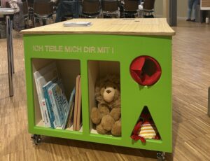 Eine bunte Holzkiste mit Plüschtieren, Büchern und verschiedenen Öffnungen.